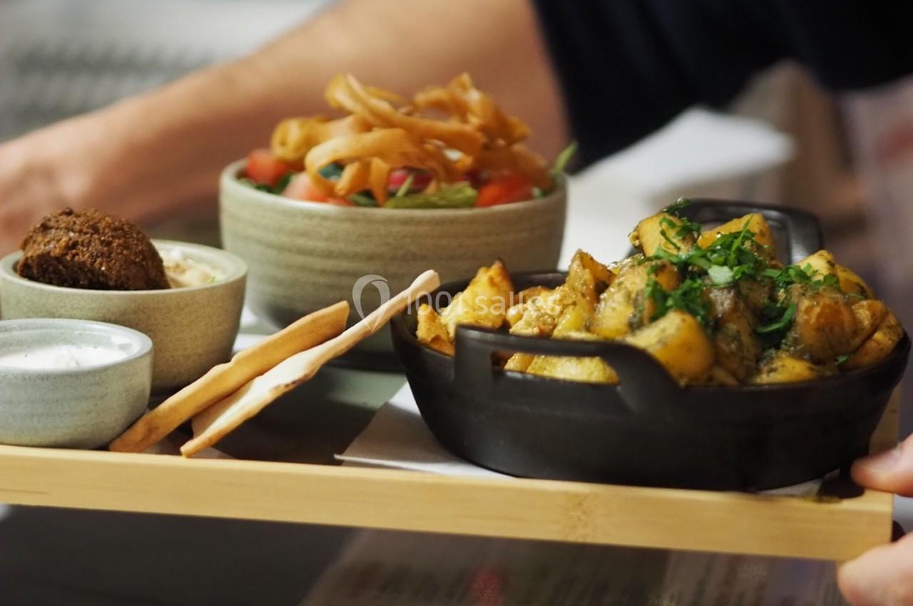 Plateau de dégustation avec pommes de terre rôties, falafels, sauces et salade colorée dans des bols en céramique.