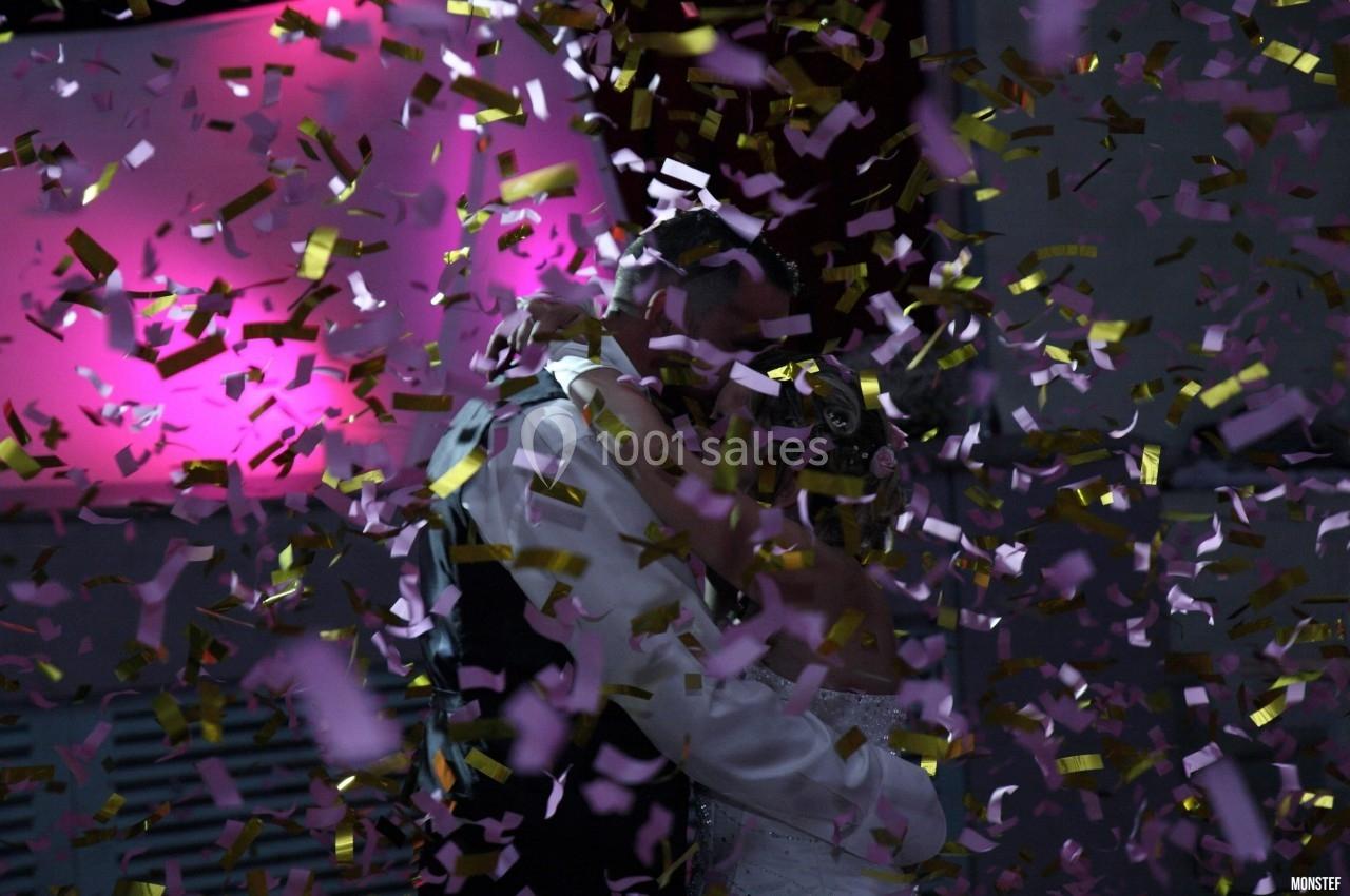 Un couple s'embrasse sous une pluie de confettis dorés et roses, avec un éclairage rose en arrière-plan.