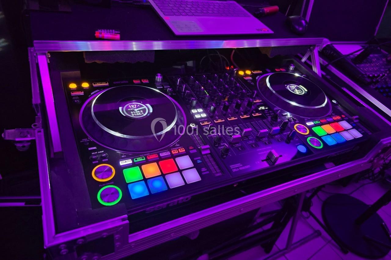 Table de mixage DJ éclairée avec des boutons colorés, deux platines et un ordinateur portable en arrière-plan.