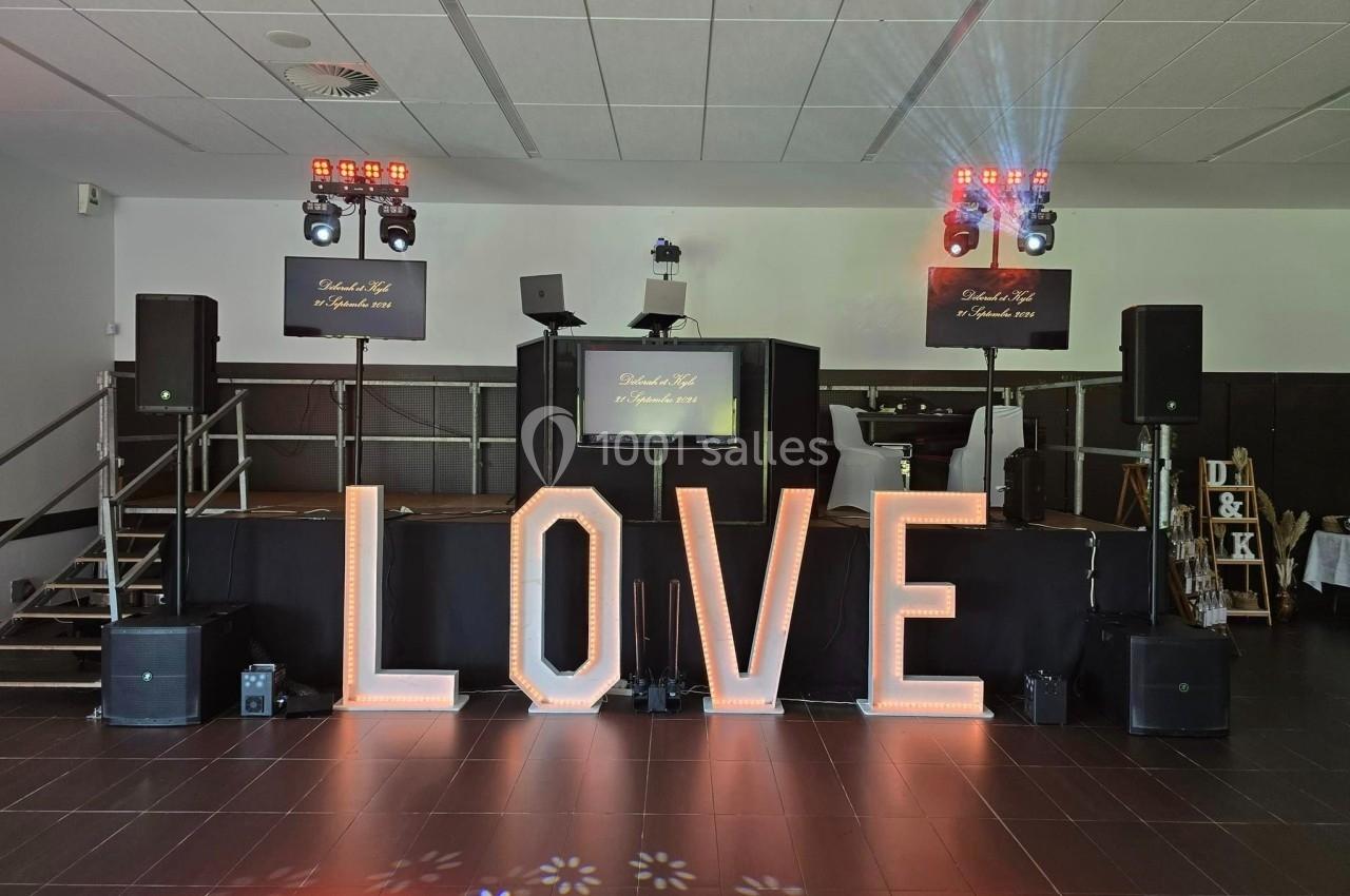Lettres lumineuses formant le mot ’LOVE’ devant une scène équipée de matériel de sonorisation et d'éclairage.