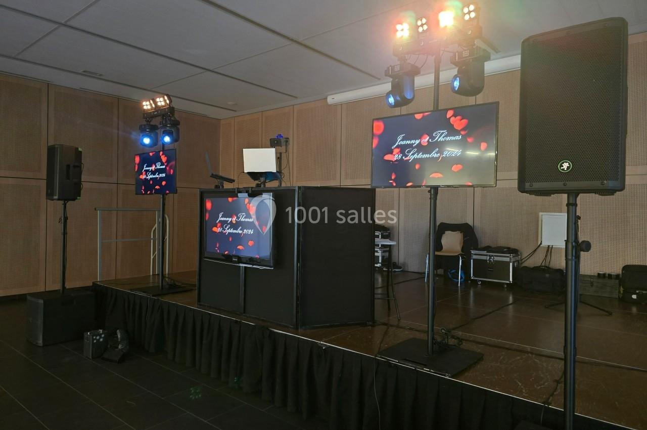 Scène de DJ avec éclairages colorés, écrans affichant des cœurs et une date, dans une salle de réception.