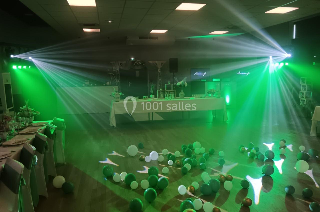 Salle de réception décorée avec des ballons au sol, éclairée par des lumières vertes et des projecteurs.