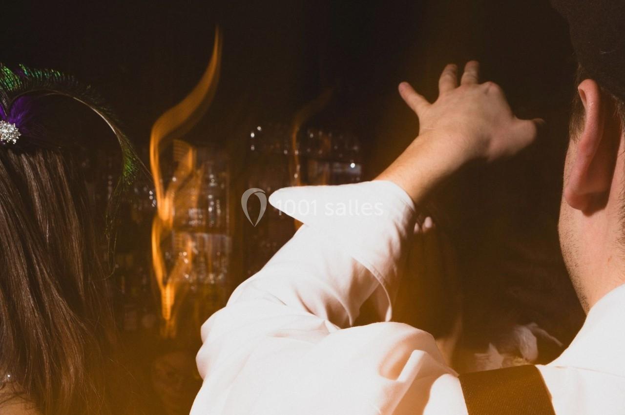 Une personne en chemise blanche lève la main dans un environnement sombre avec des lumières floues en arrière-plan.