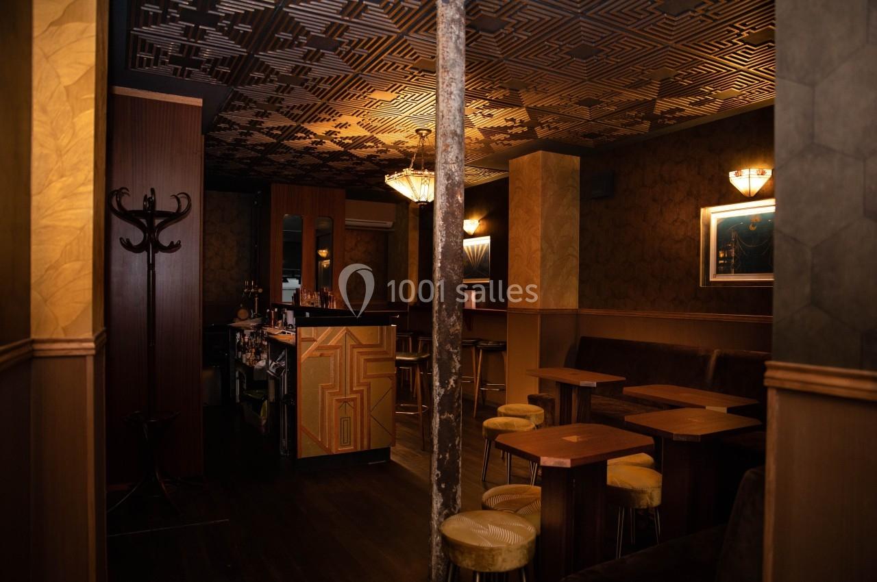 Intérieur d'un bar avec tables en bois, tabourets rembourrés, éclairage tamisé et décoration murale géométrique.