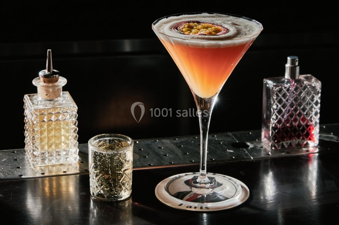 Verre à cocktail élégant garni d'un demi-fruit de la passion, posé sur un bar avec des accessoires de mixologie.