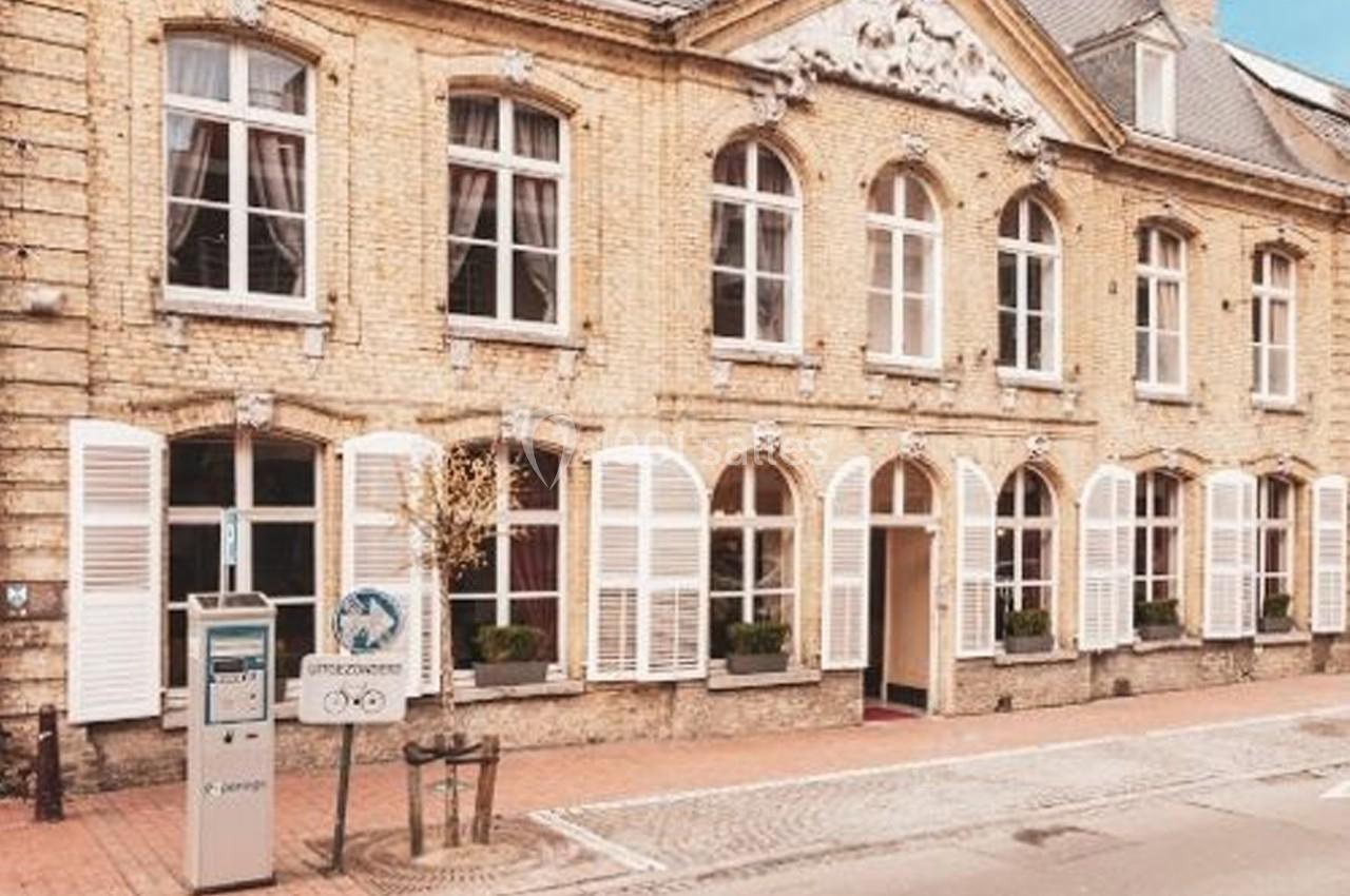 Façade en briques d'un bâtiment ancien avec volets blancs, fenêtres cintrées et une borne de stationnement au premier plan.