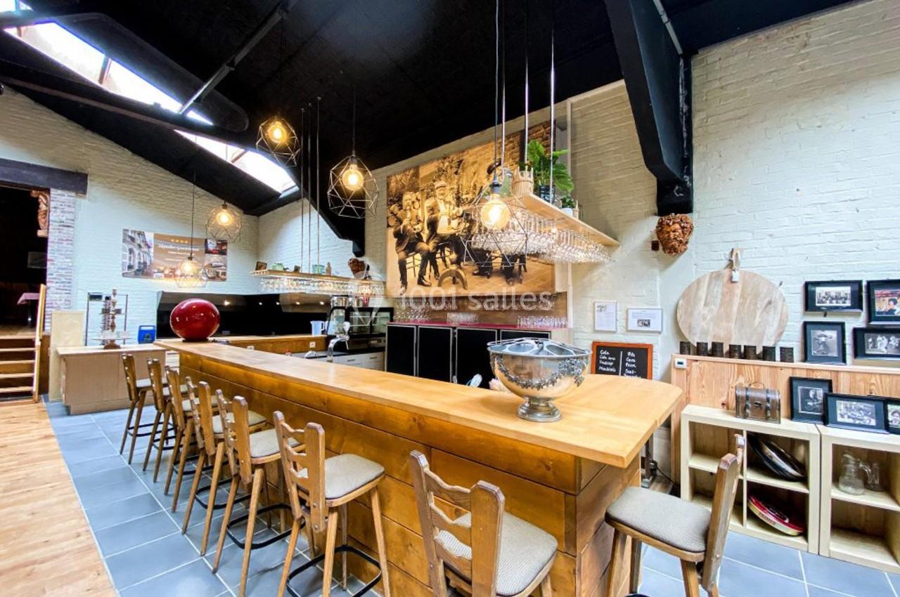 Bar en bois avec des tabourets alignés, éclairage suspendu et décorations murales dans un espace lumineux avec plafond noir.