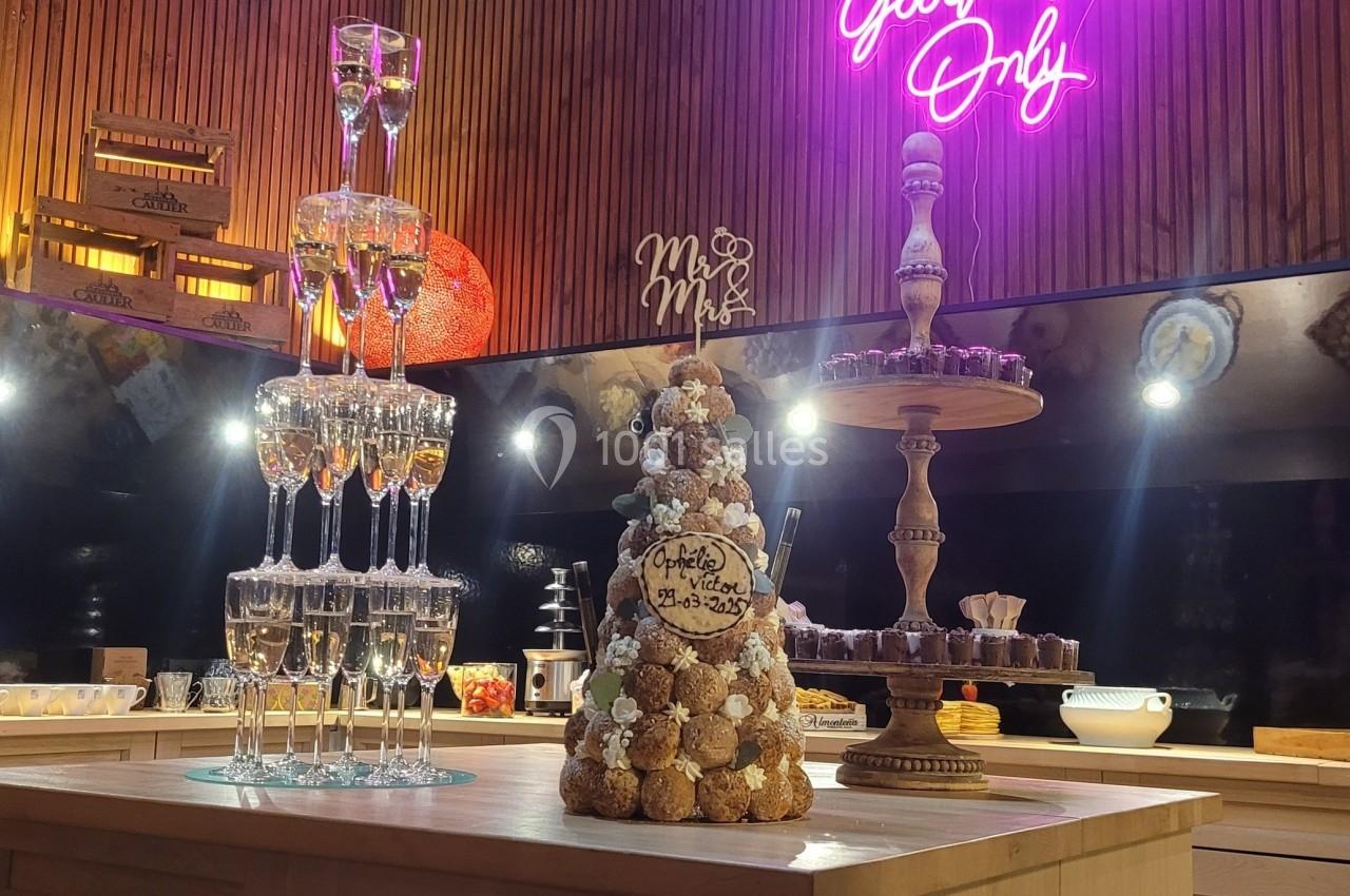 Tour de coupes de champagne et pièce montée en choux sur une table, dans une salle décorée avec éclairage néon.