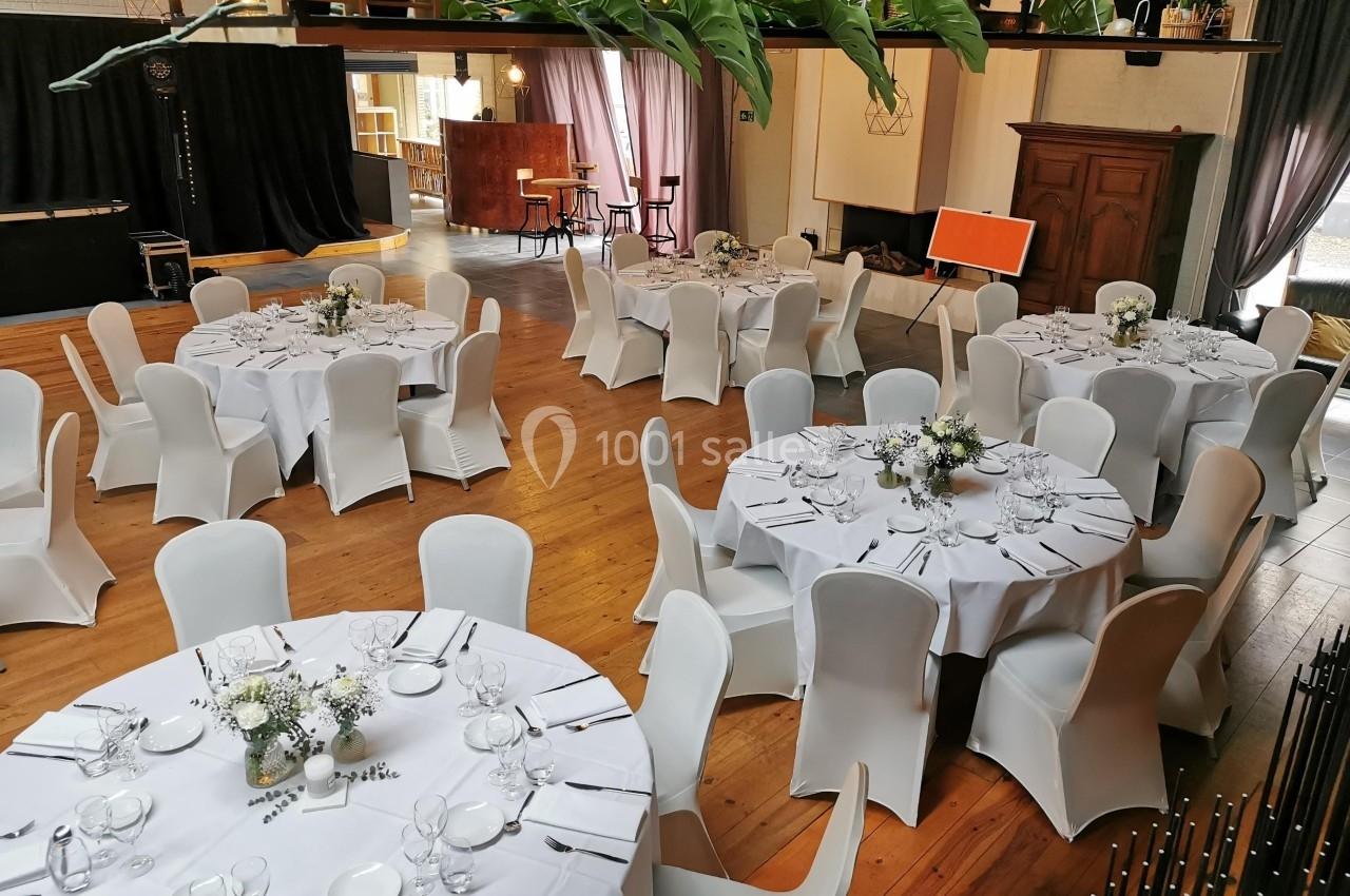 Salle de réception avec tables rondes dressées, nappes blanches et décorations florales, dans un espace lumineux et…