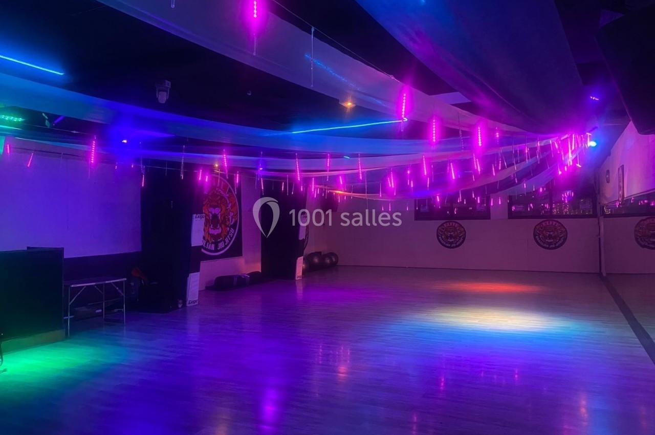 Salle de danse avec éclairage coloré violet et bleu, sol en parquet et murs décorés de motifs.