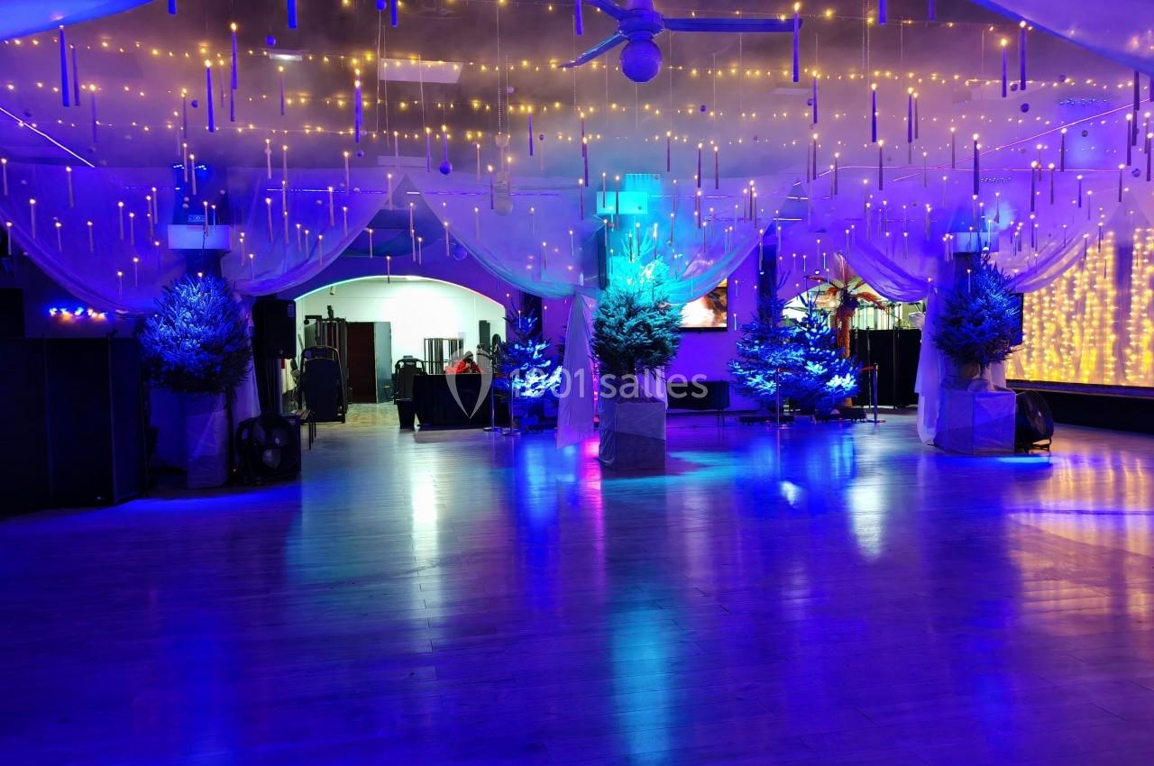 Salle décorée avec des guirlandes lumineuses, des sapins illuminés et des voilages suspendus, ambiance festive.