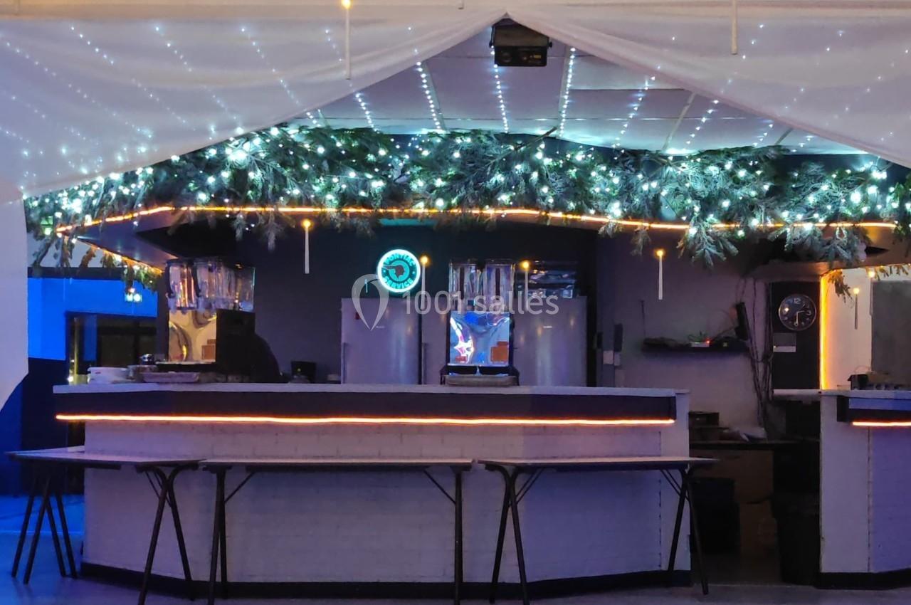 Bar décoré avec des guirlandes lumineuses et des branches de sapin, sous un plafond étoilé et un éclairage tamisé.