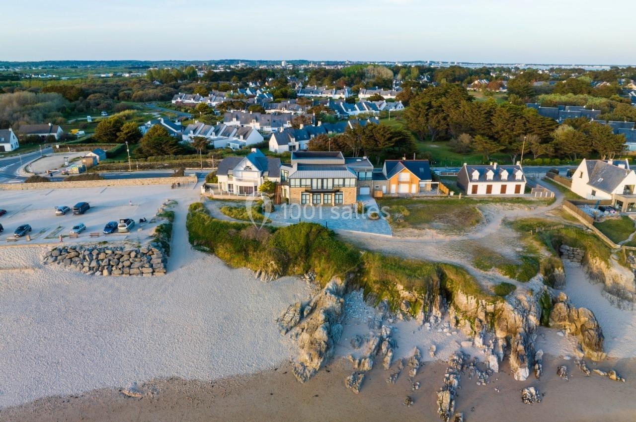 Vue aérienne d'une plage bordée de falaises avec des maisons et un parking à proximité, dans un paysage côtier.