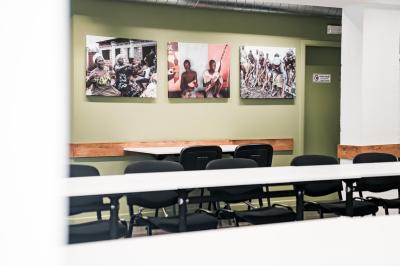 Personnes assises à des tables sur une terrasse en bois, entourée de verdure et d'immeubles modernes en arrière-plan.