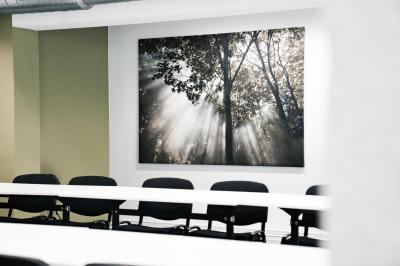 Personnes assises à des tables sur une terrasse en bois, entourée de verdure et d'immeubles modernes en arrière-plan.
