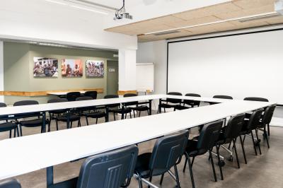 Personnes assises à des tables sur une terrasse en bois, entourée de verdure et d'immeubles modernes en arrière-plan.