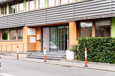 Personnes assises à des tables sur une terrasse en bois, entourée de verdure et d'immeubles modernes en arrière-plan.