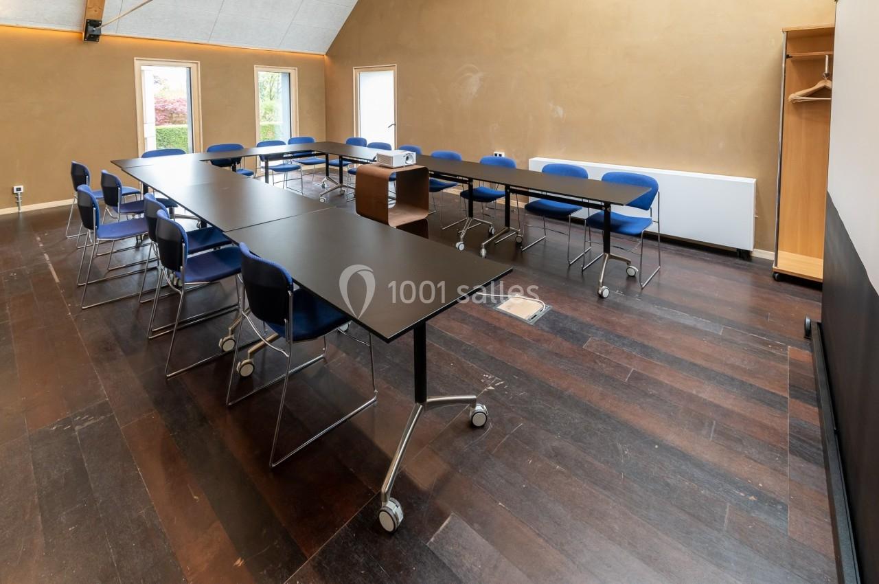 Salle de réunion lumineuse avec tables noires sur roulettes, chaises bleues et parquet sombre.