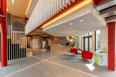 Bâtiment moderne avec façade en verre et briques, entouré de végétation et d'une allée pavée.