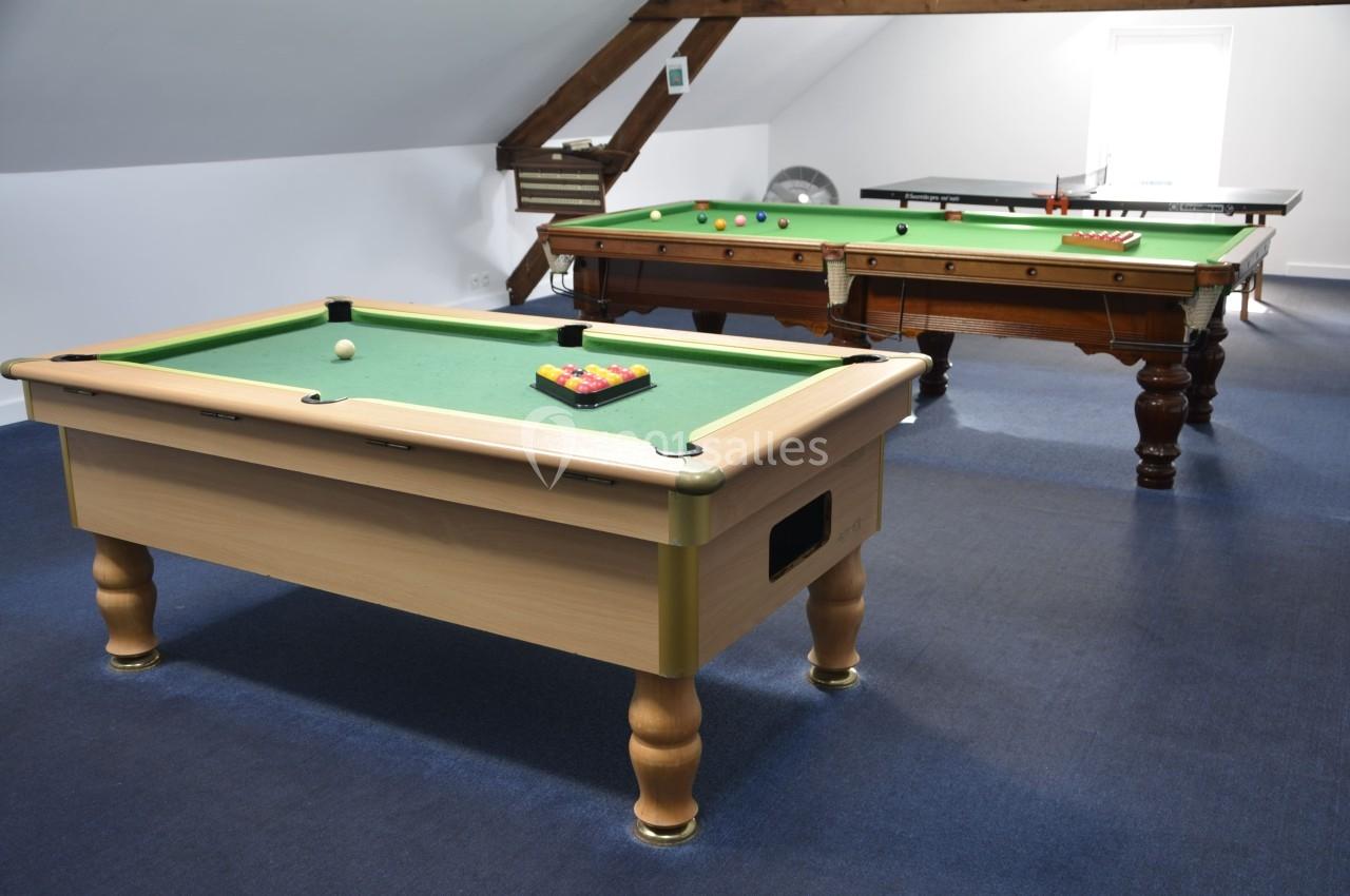 Tables de billard dans une salle aménagée sous les combles, avec tapis verts et accessoires de jeu.