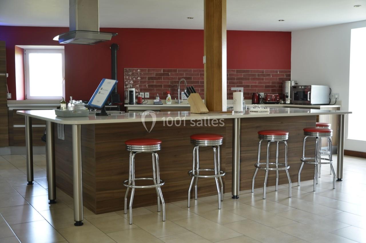 Cuisine moderne avec un îlot central en bois, tabourets métalliques rouges et mur en briques rouges.