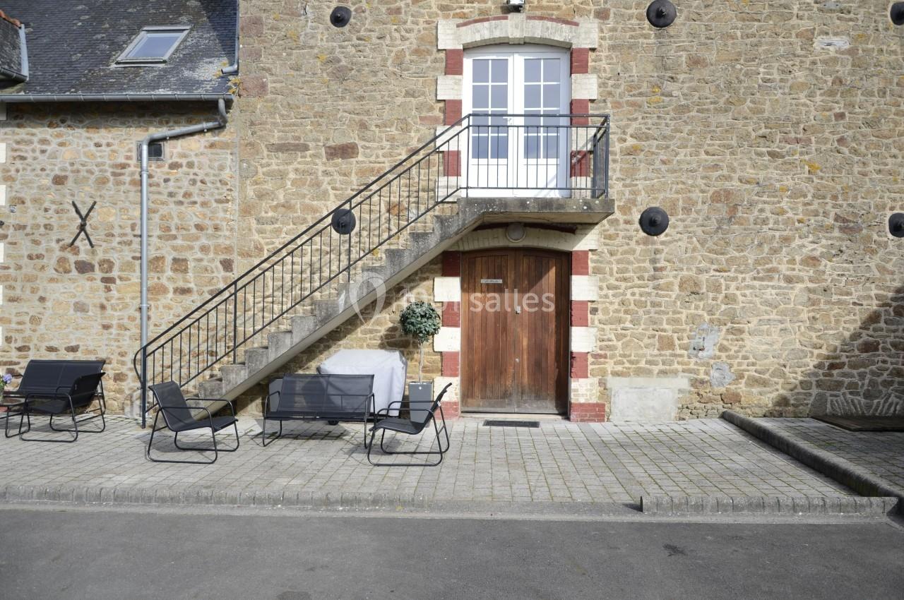 Façade en pierre avec escalier extérieur menant à une porte-fenêtre, mobilier de jardin sur le trottoir.