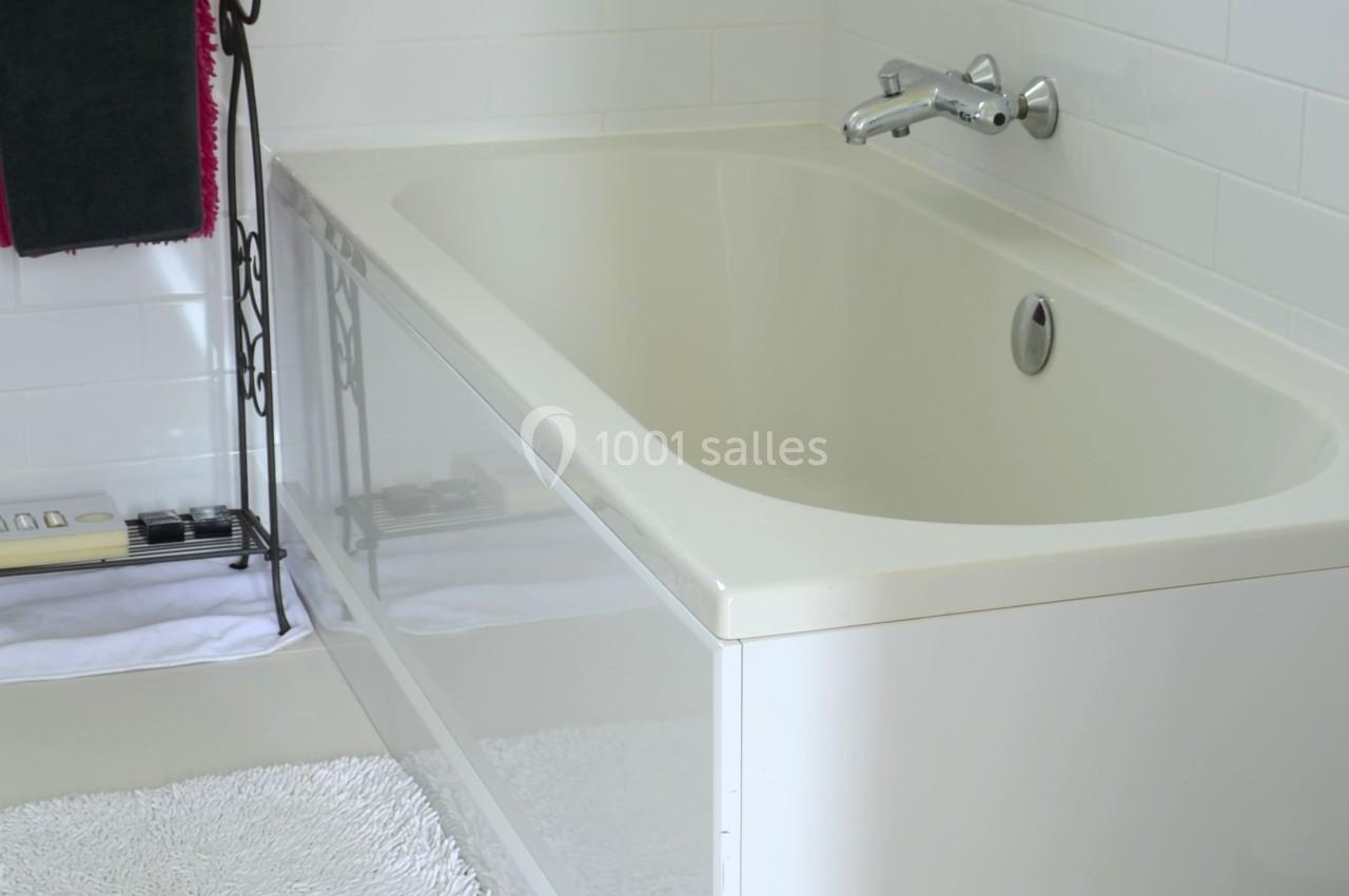 Baignoire blanche avec robinet mural, entourée de carrelage blanc et d'un porte-serviettes noir avec une serviette.