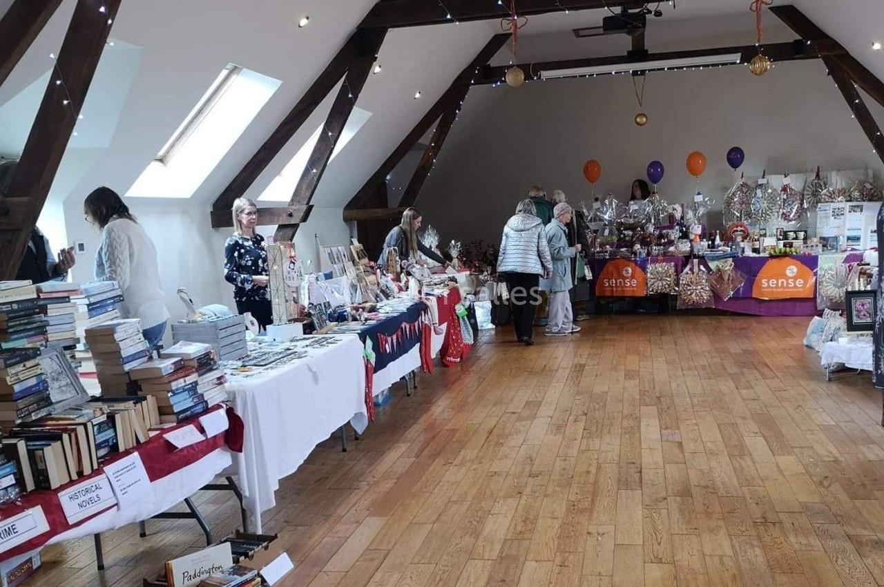 Salle avec des stands de livres, décorations et artisanat, des personnes discutent et explorent les articles exposés.
