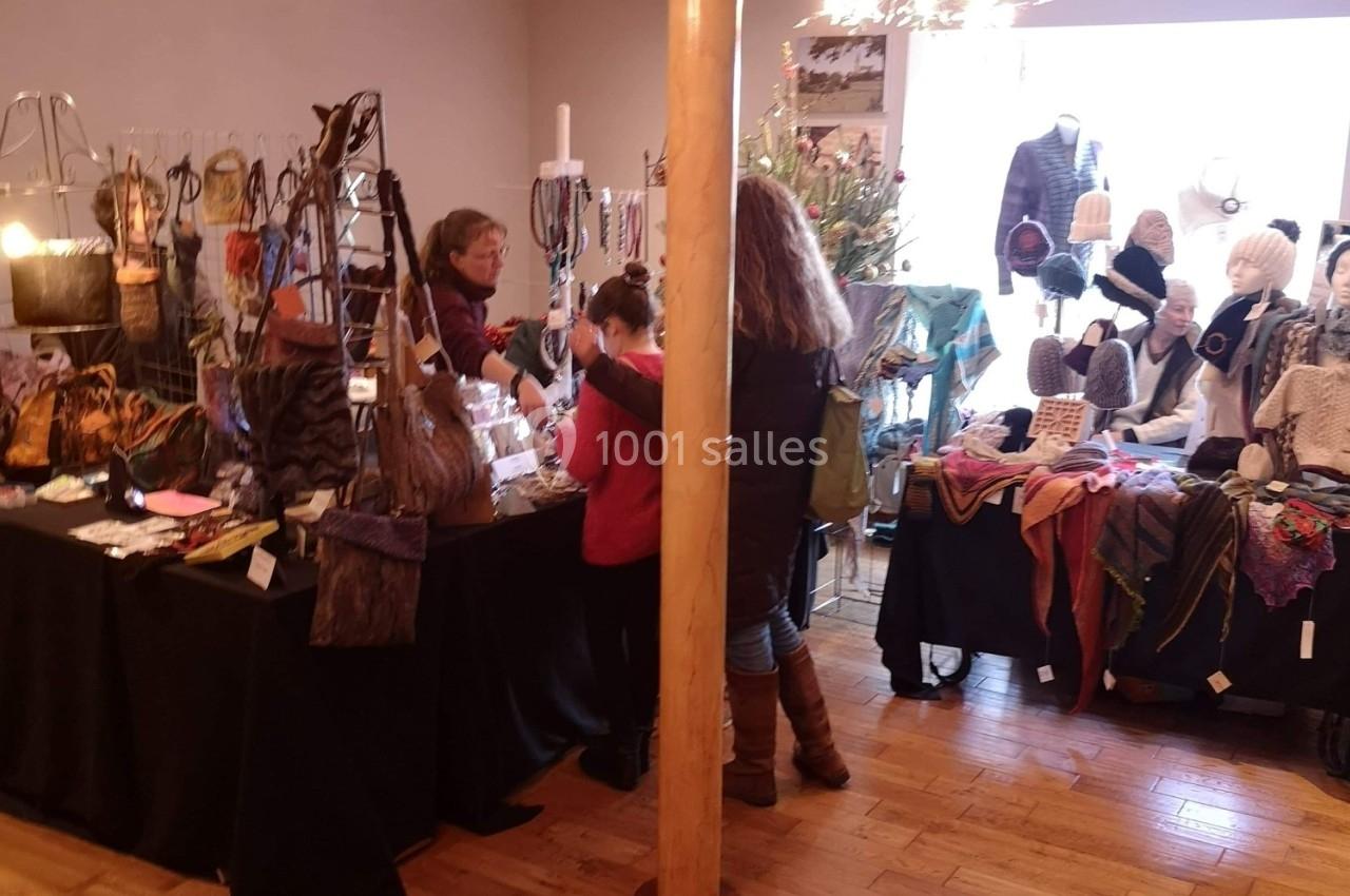 Des personnes regardent des articles artisanaux exposés sur des tables dans un marché intérieur.