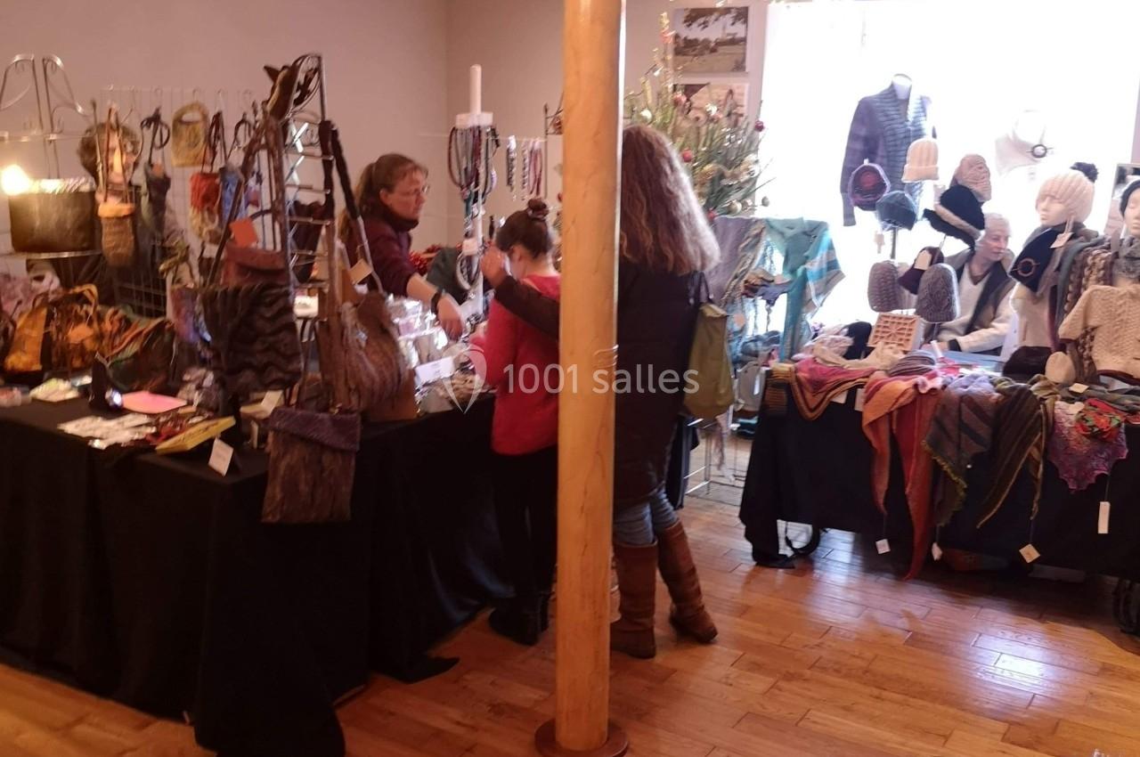 Stand d'artisanat avec accessoires en laine et tissus colorés, deux femmes et une enfant discutant avec une vendeuse.