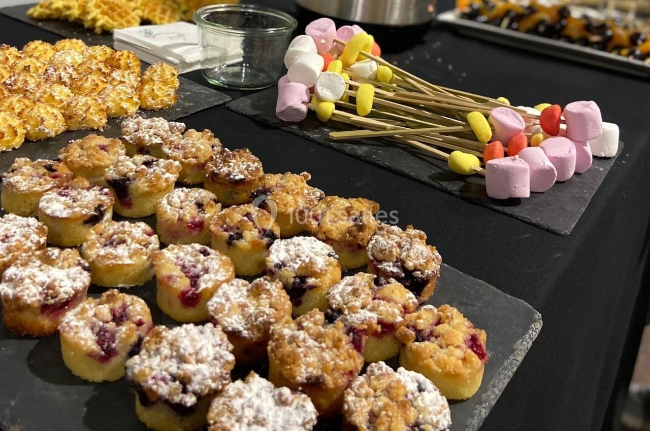 Plateau de desserts variés comprenant des muffins, des brochettes de guimauves et des pâtisseries sur une table noire.