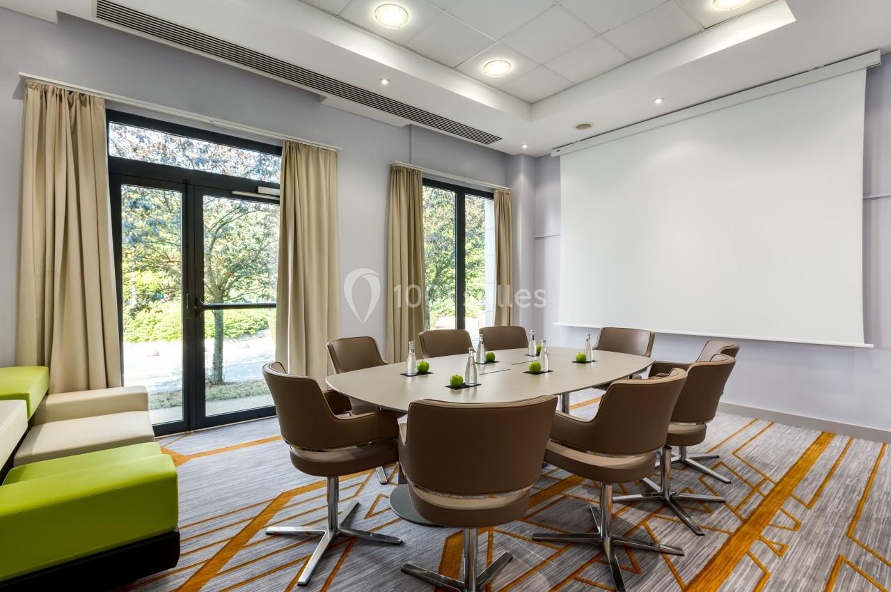 Salle de réunion lumineuse avec table ovale, chaises modernes, rideaux beiges et écran de projection.