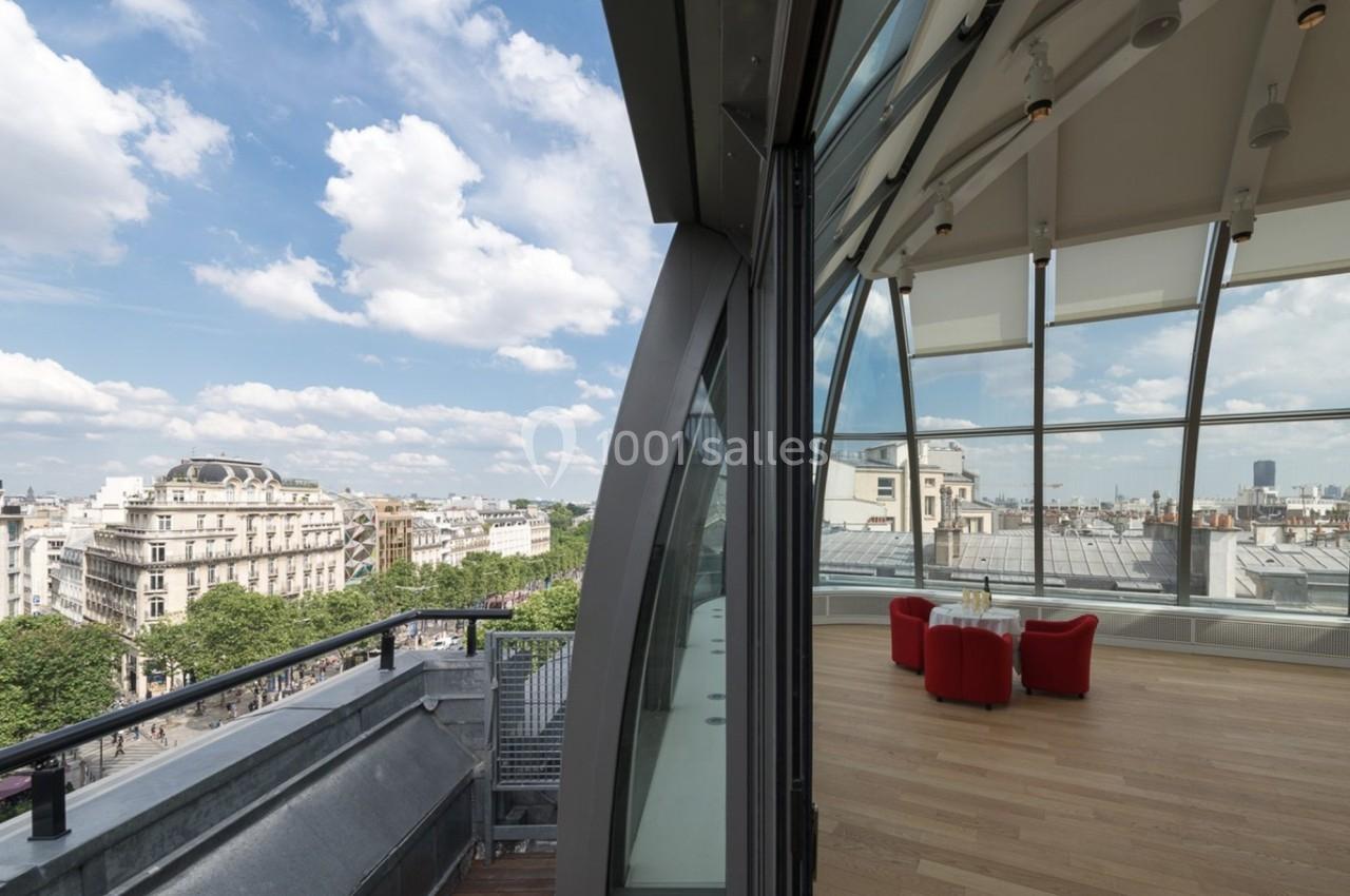 Vue d'une terrasse urbaine et d'un espace intérieur vitré avec parquet, offrant une perspective sur des bâtiments parisiens.