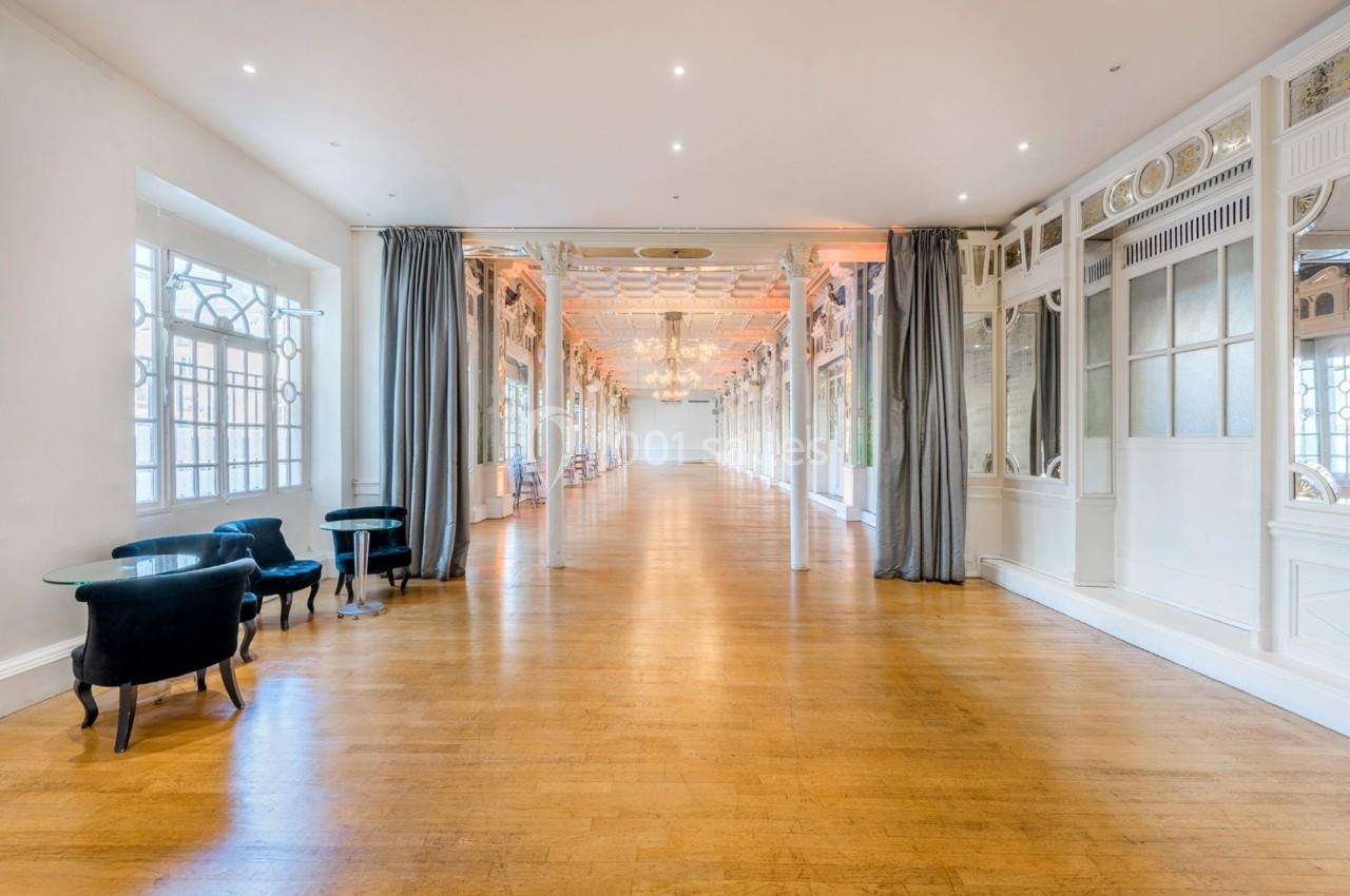 Salle lumineuse avec parquet en bois, grandes fenêtres, miroirs décoratifs et rideaux gris.