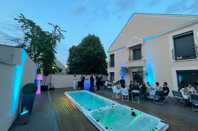 Tente blanche avec parois transparentes installée en extérieur sur un sol gravillonné, entourée d'arbres.