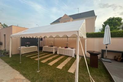 Tente blanche avec parois transparentes installée en extérieur sur un sol gravillonné, entourée d'arbres.