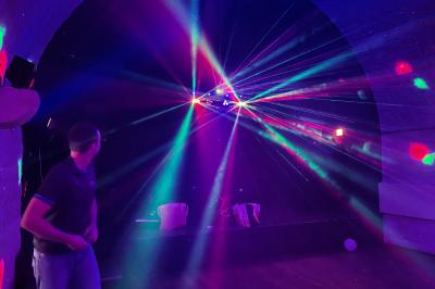 Tente blanche avec parois transparentes installée en extérieur sur un sol gravillonné, entourée d'arbres.