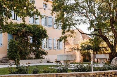Miniature Justine Compagnon Wedding #12 Façade d'une maison ancienne avec volets bleus, entourée de végétation et éclairée par des guirlandes lumineuses.
