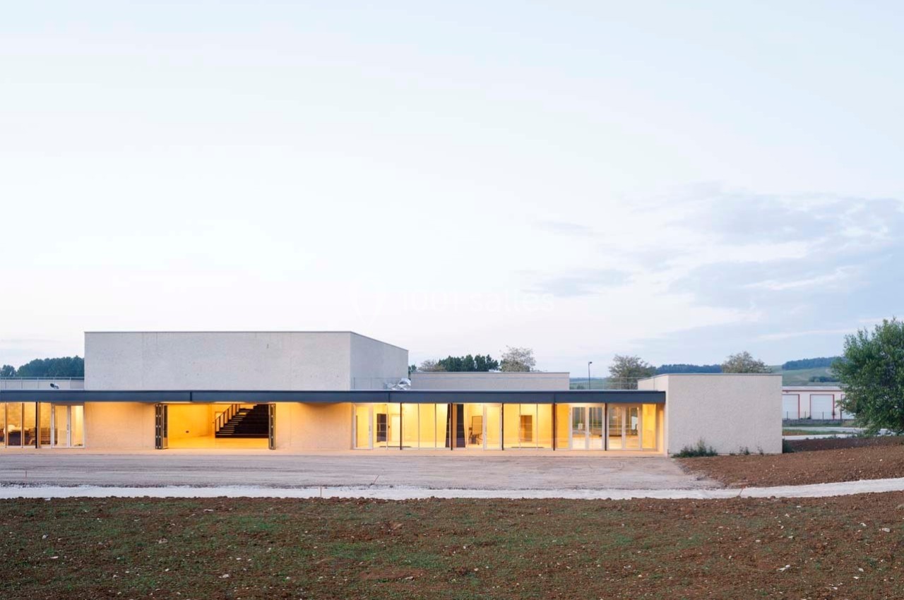 Bâtiment moderne à un étage avec façade vitrée, éclairé de l'intérieur, entouré de terrain dégagé.