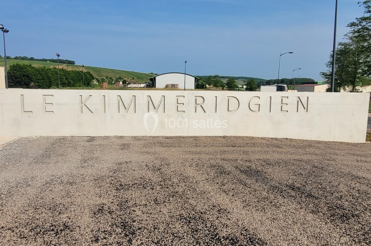 Mur en béton avec l'inscription ’Le Kimméridgien’, situé dans un environnement rural sous un ciel dégagé.
