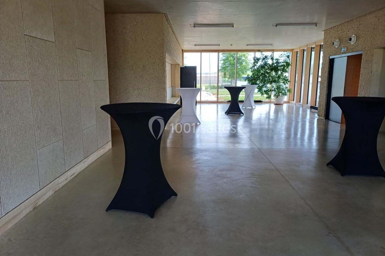 Salle lumineuse avec tables hautes recouvertes de nappes noires et blanches, grandes fenêtres et plantes en arrière-plan.