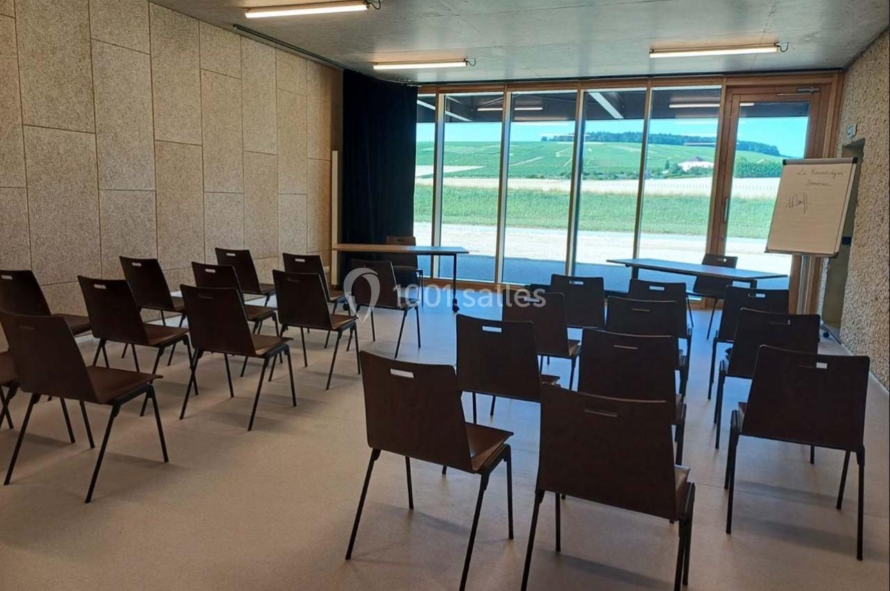 Salle de réunion lumineuse avec des chaises disposées en rangées, un tableau blanc et une vue sur la campagne.