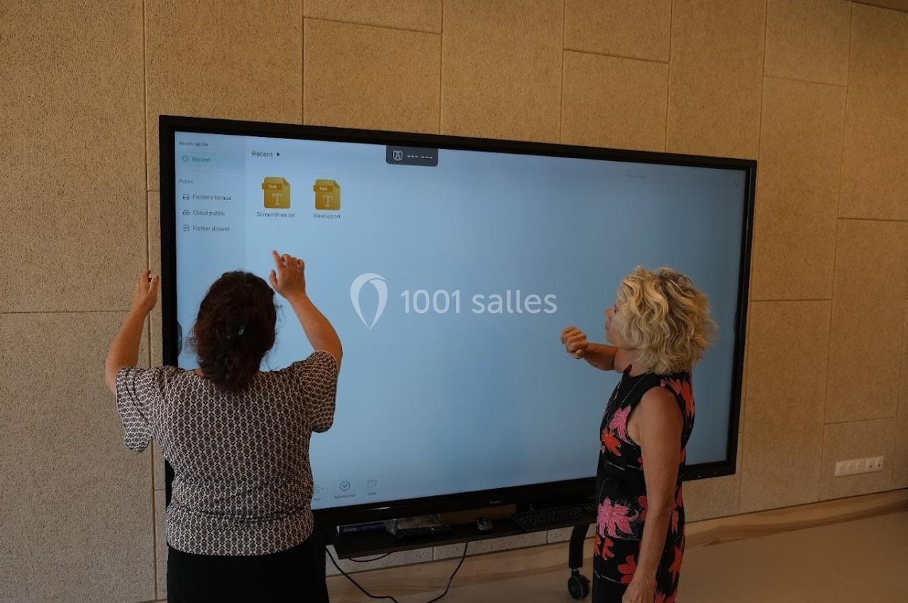 Deux femmes interagissent avec un grand écran tactile affichant des dossiers numériques dans une salle moderne.