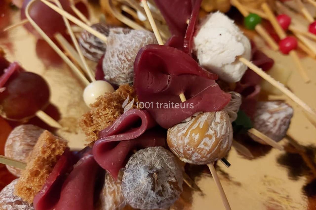 Brochettes apéritives composées de charcuterie, figues séchées, fromage frais et morceaux de pain sur un plateau doré.