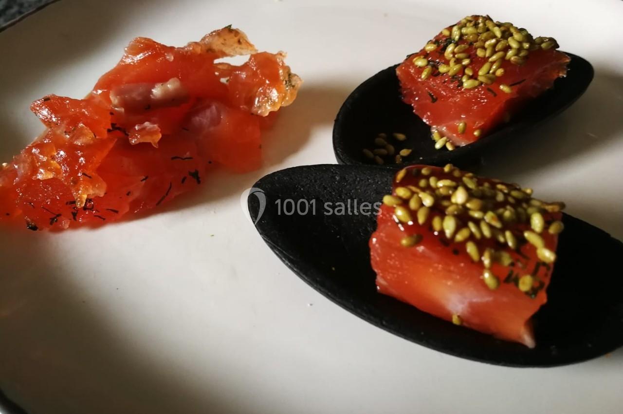 Assiette avec du saumon mariné et des morceaux garnis de graines de sésame sur des cuillères noires.