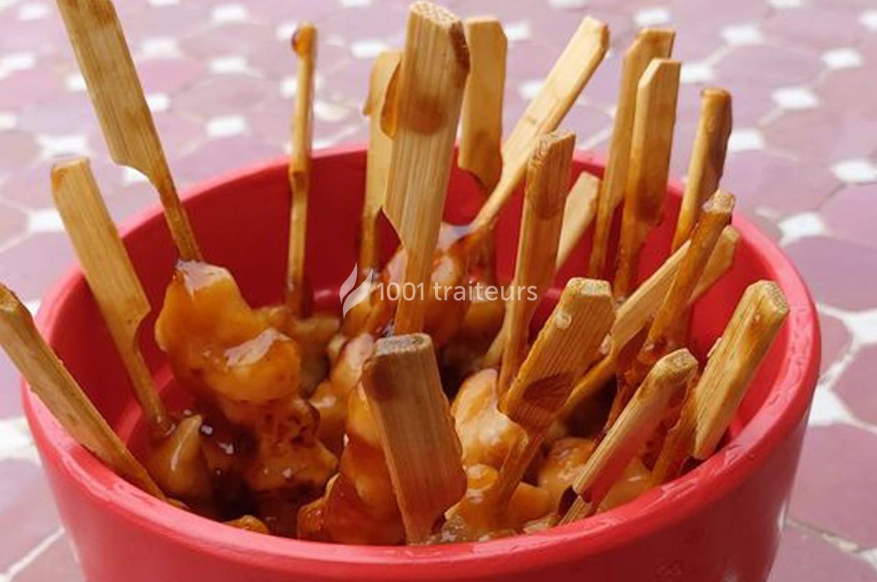 Brochettes de poulet glacées à la sauce, présentées dans un bol rouge sur une table aux motifs géométriques.
