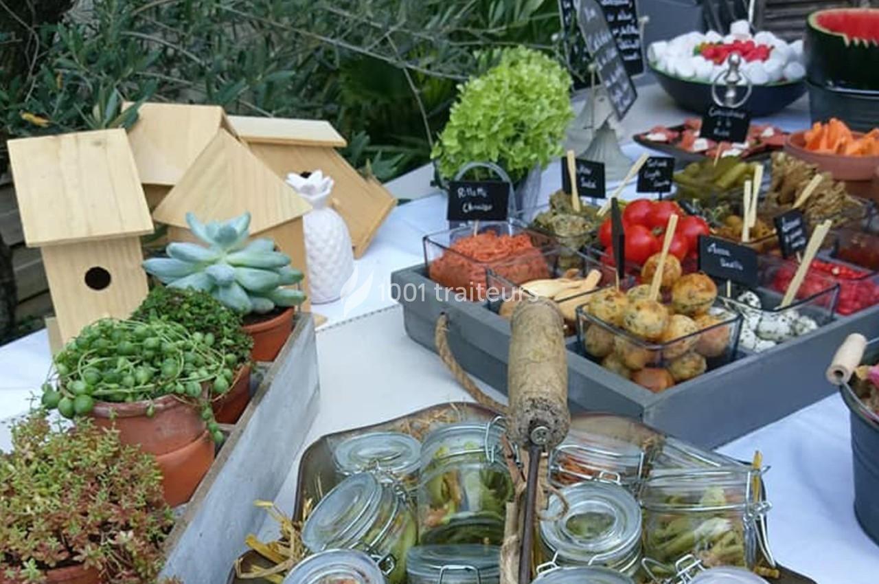 Buffet en plein air avec divers plats, condiments, légumes, pots de plantes et décorations en bois.