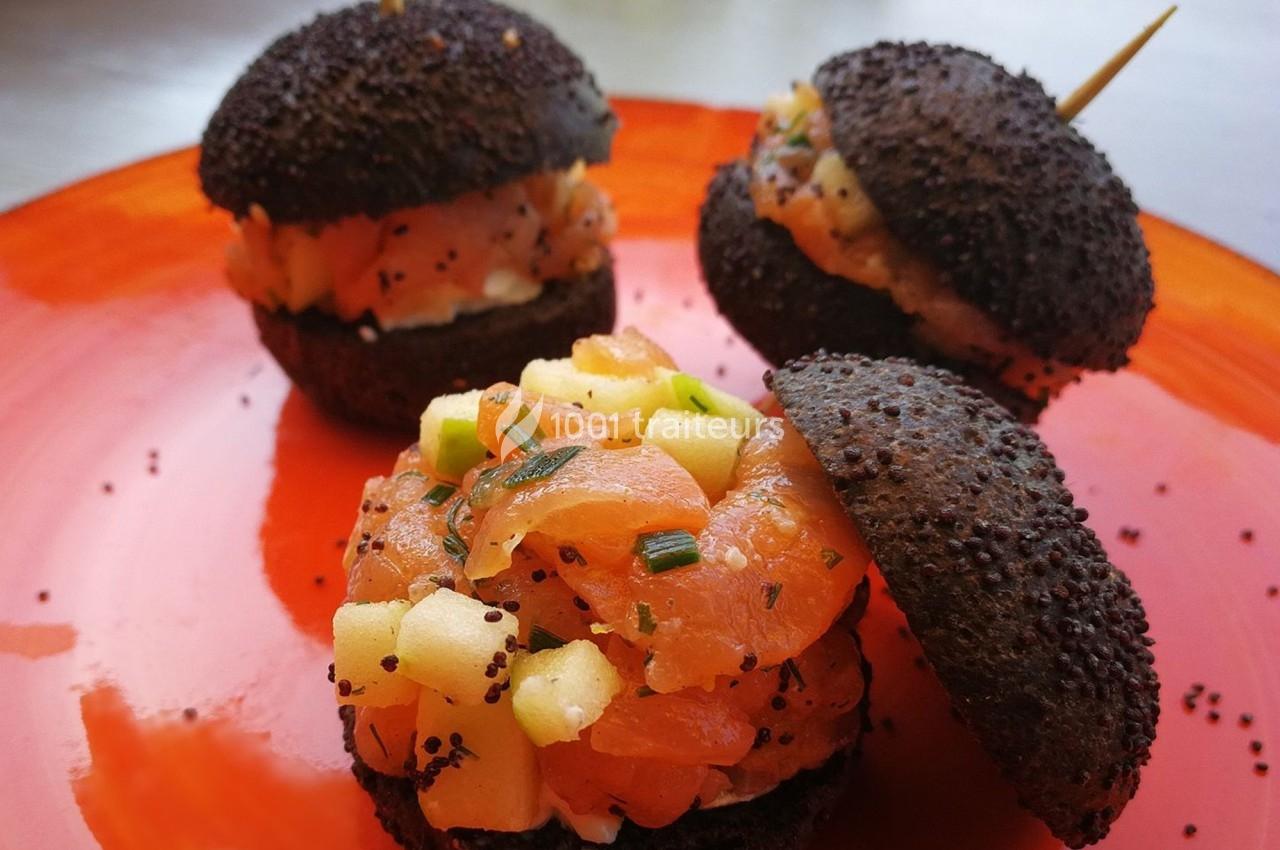 Mini-burgers au pain noir garnis de tartare de saumon, pommes et ciboulette, présentés sur une assiette orange.