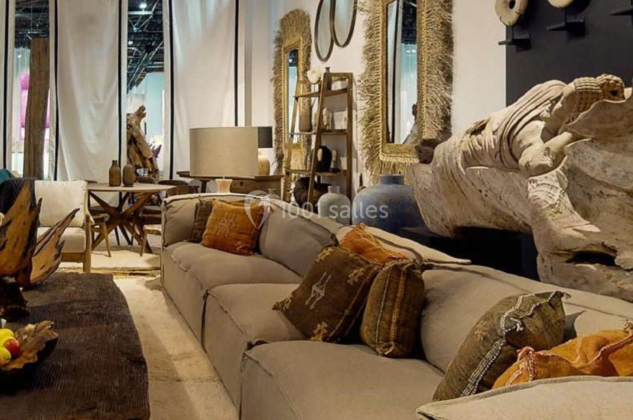 Canapé beige avec coussins décoratifs dans un salon aménagé avec des objets en bois et des miroirs encadrés.