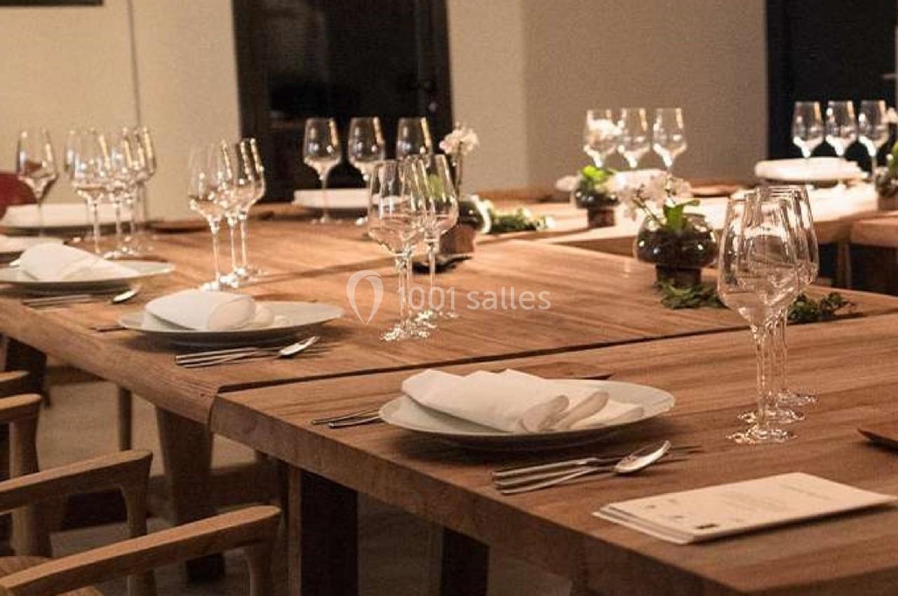 Table en bois dressée avec des assiettes, serviettes pliées, couverts et verres, dans une salle élégamment éclairée.